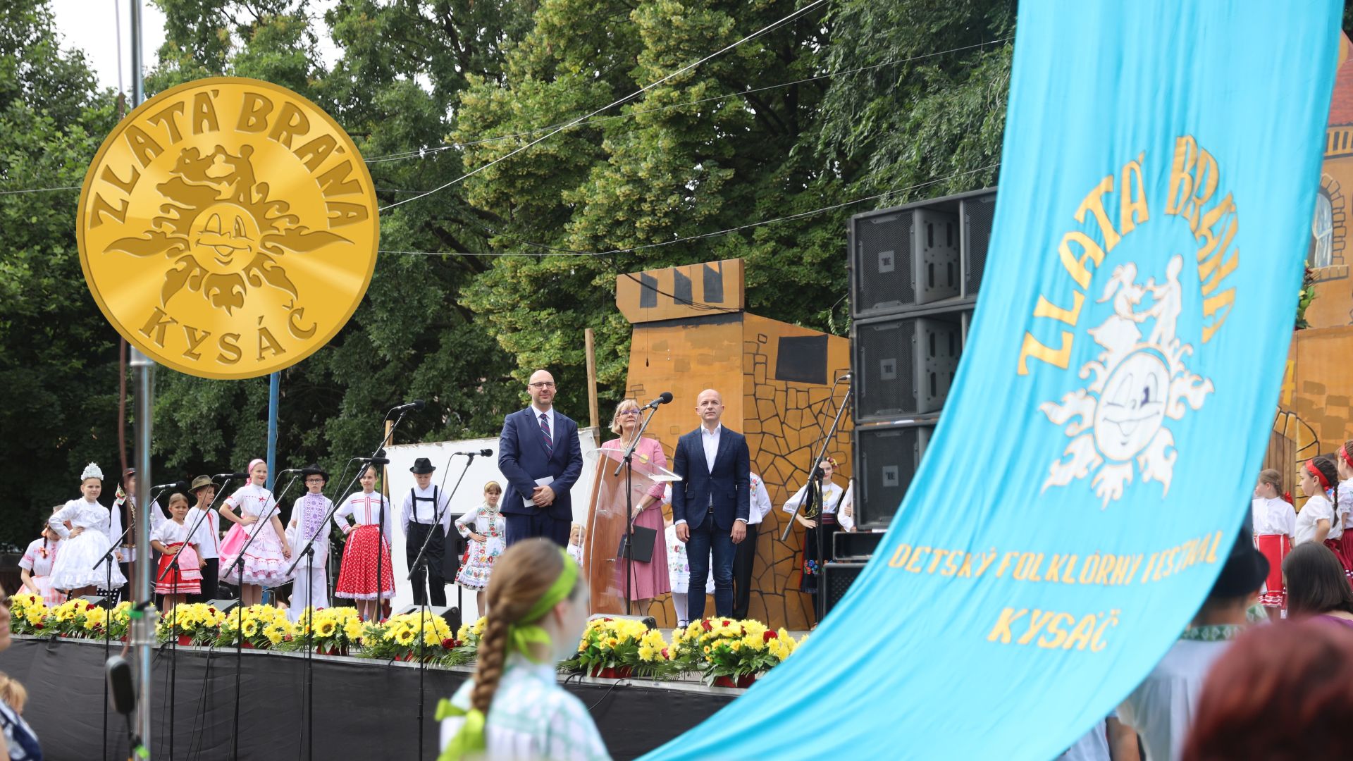 Dečji folklorni fetival u Kisaču - svečano otvaranje, deca u nošnji i gosti, zastava i znak festivala.